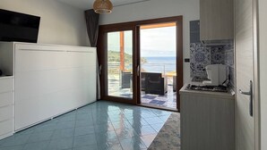 Een keuken met uitzicht op zee, een eethoek met tafel en stoelen, en een schuifdeur naar een terras.