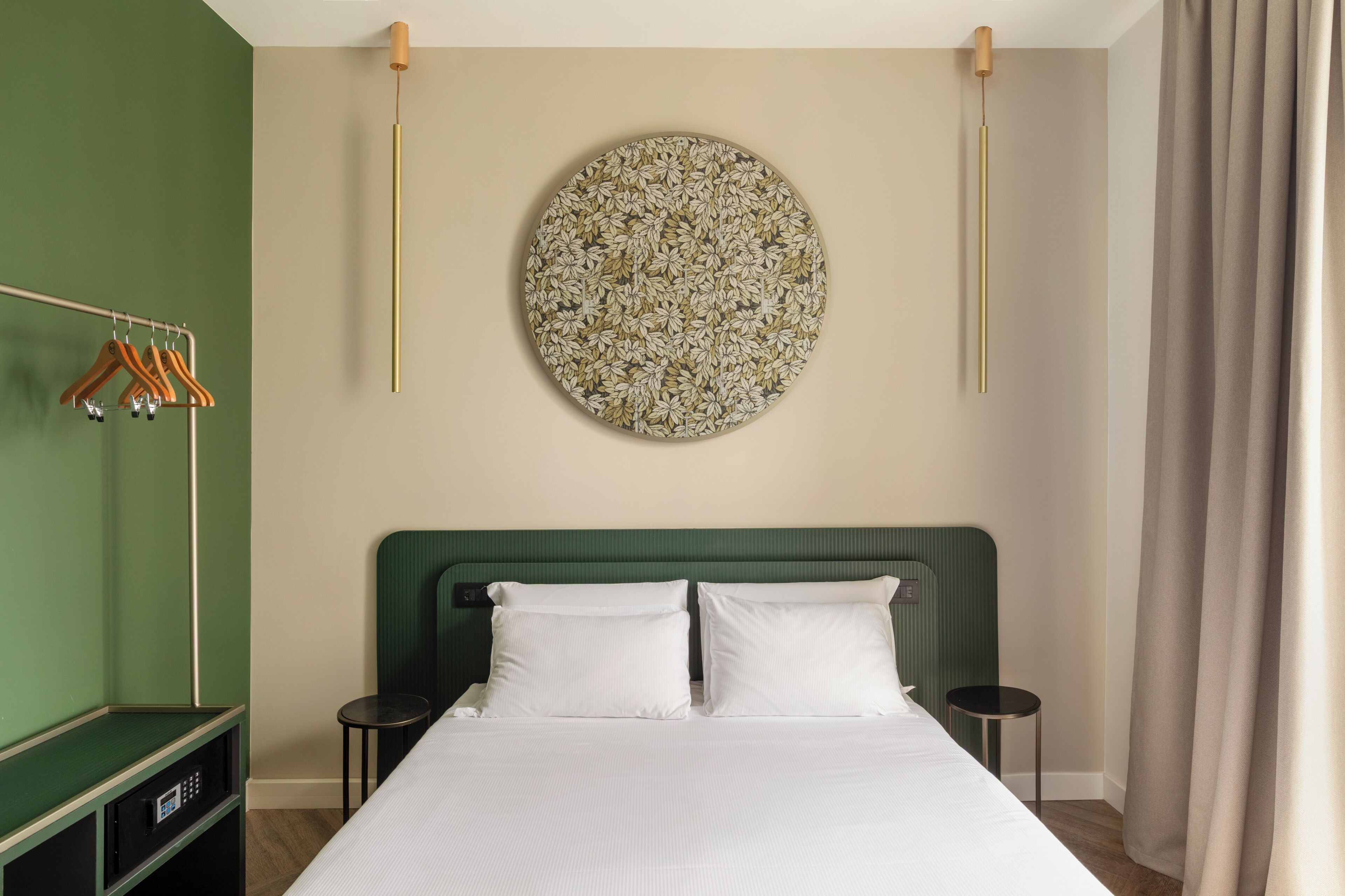 Une chambre d’hôtel avec un lit, deux tables de chevet, un mur vert, un élément de décoration murale rond et un porte-manteau.