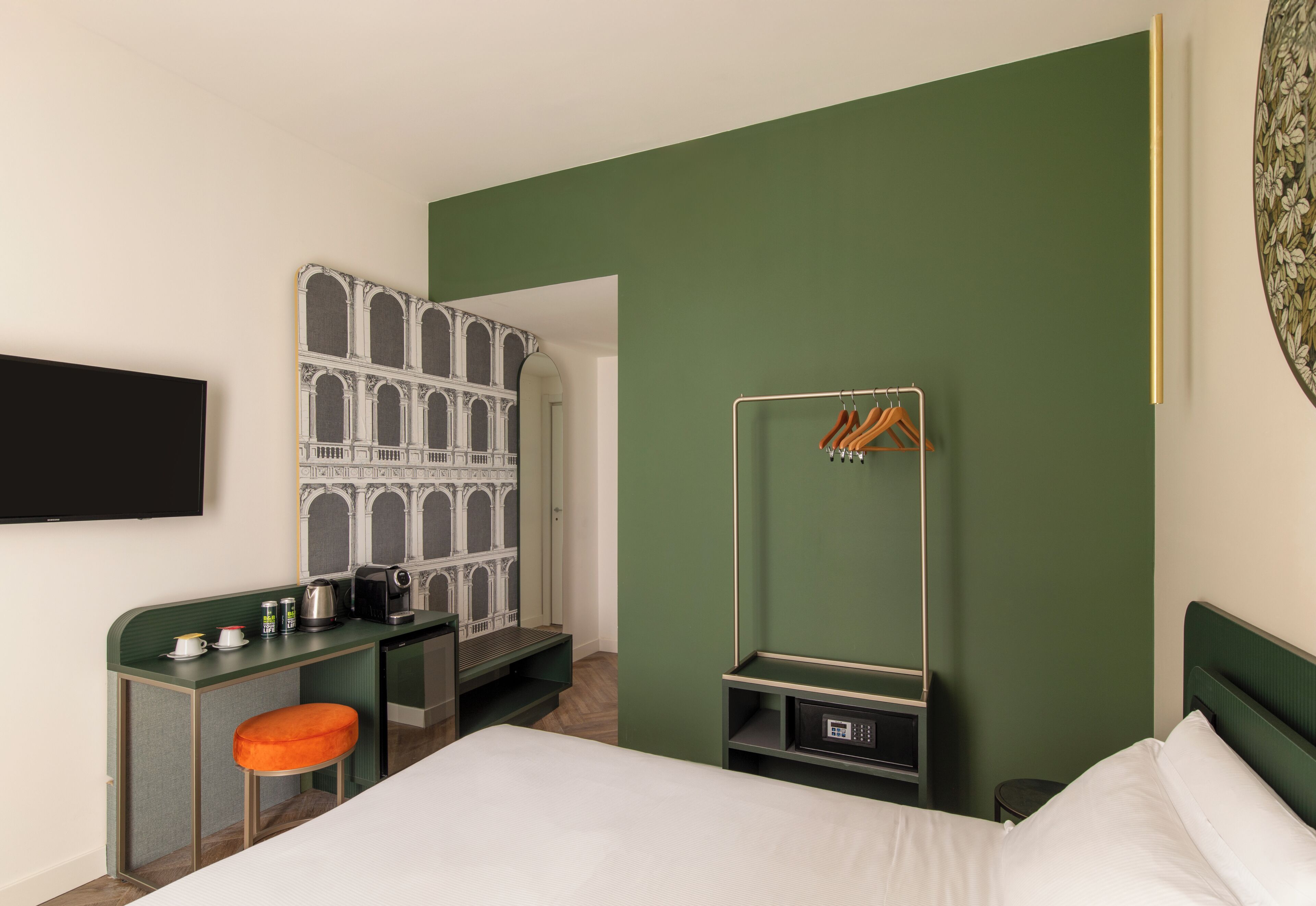 A hotel room with a bed, a desk with a chair, a wardrobe, and a coat rack.