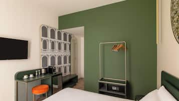 Una habitación de hotel con una cama, un escritorio con silla, un armario y un perchero.