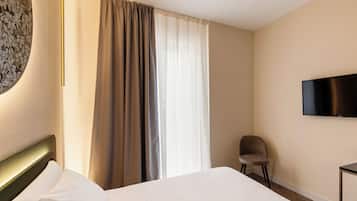 A hotel room with a bed, a chair, a TV, and a window with curtains.
