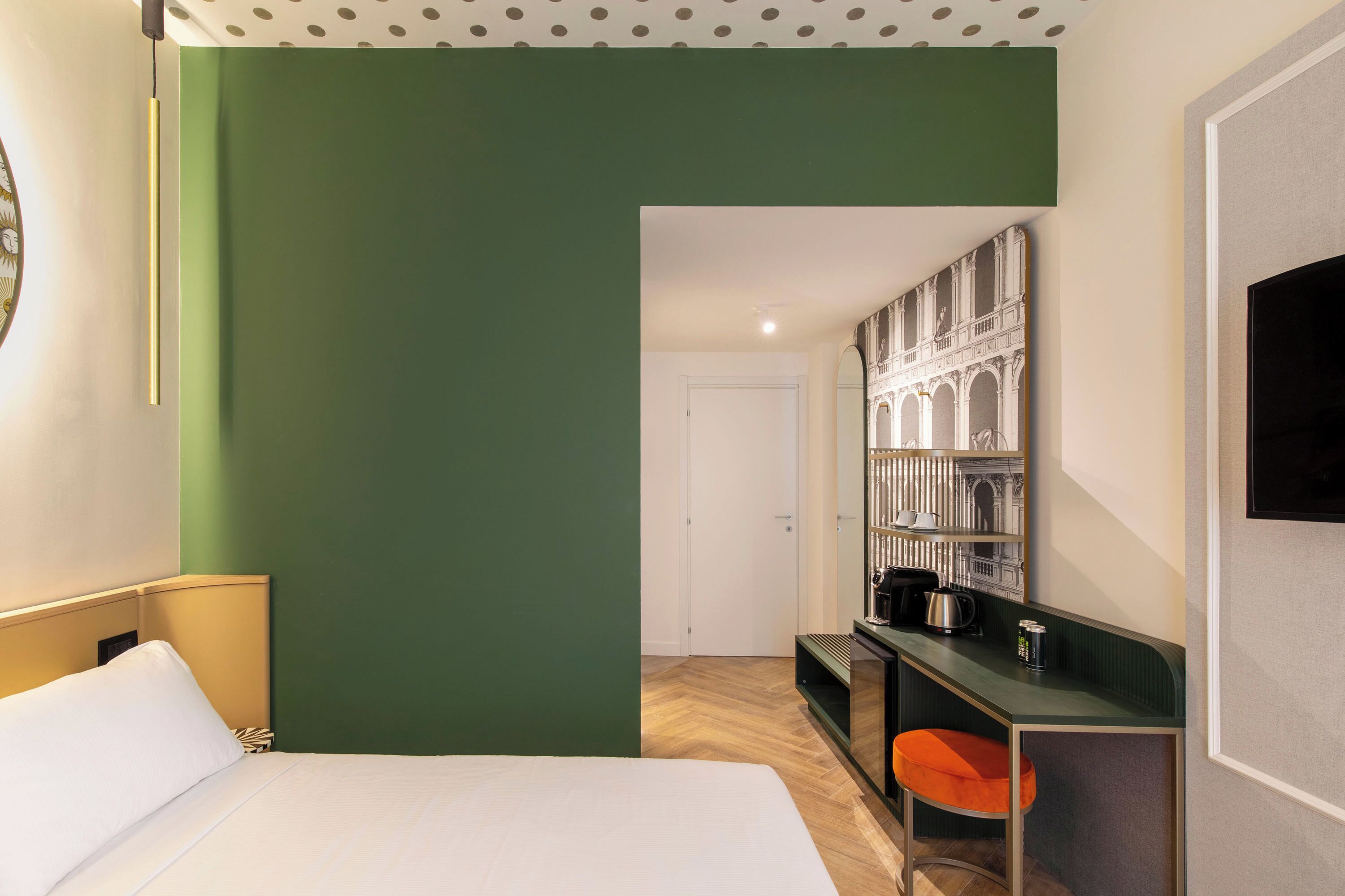 A hotel room with a bed, a desk with a chair, a bookshelf, and a television.