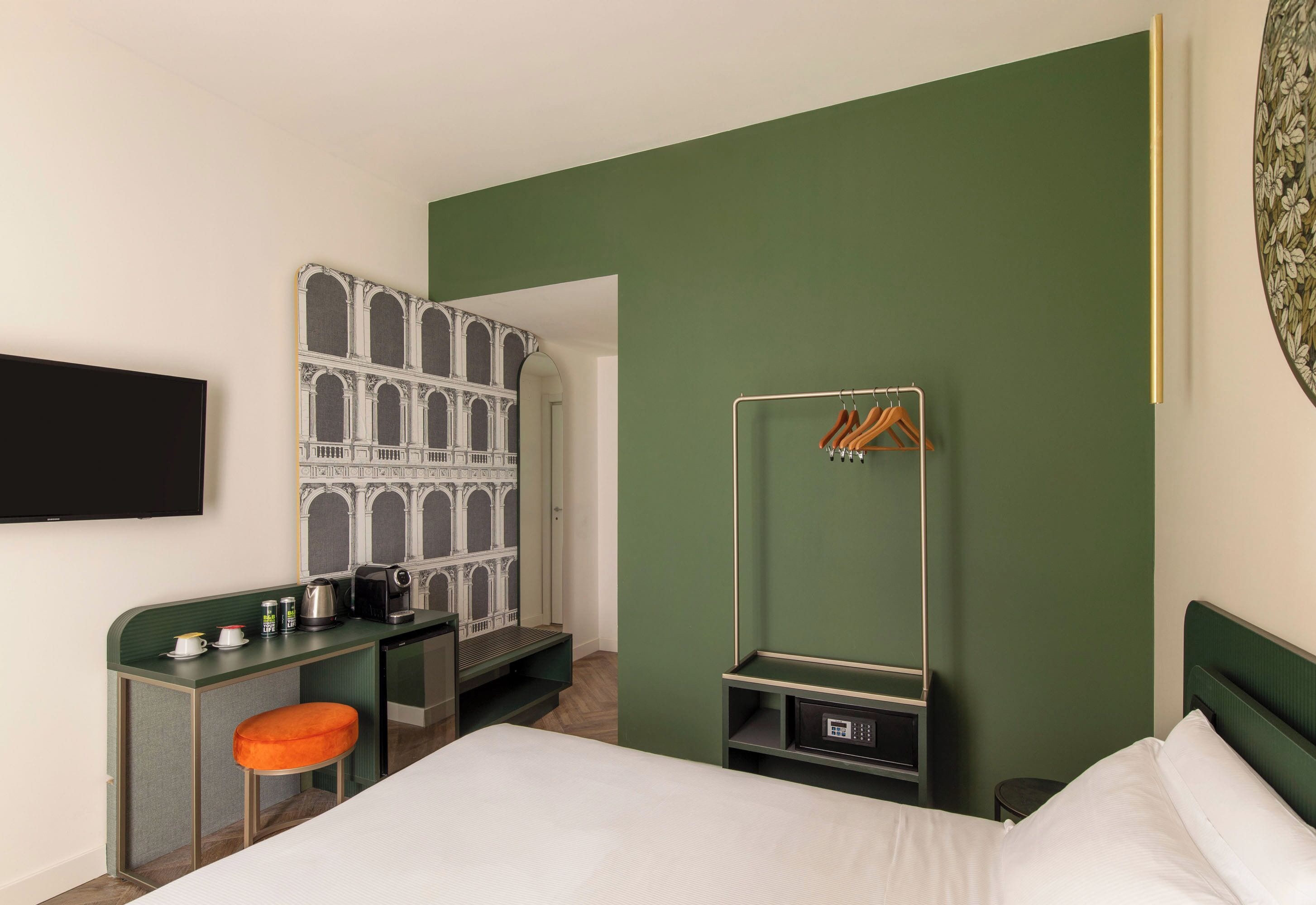 A hotel room with a bed, a desk with a chair, a coat rack, and a wardrobe.