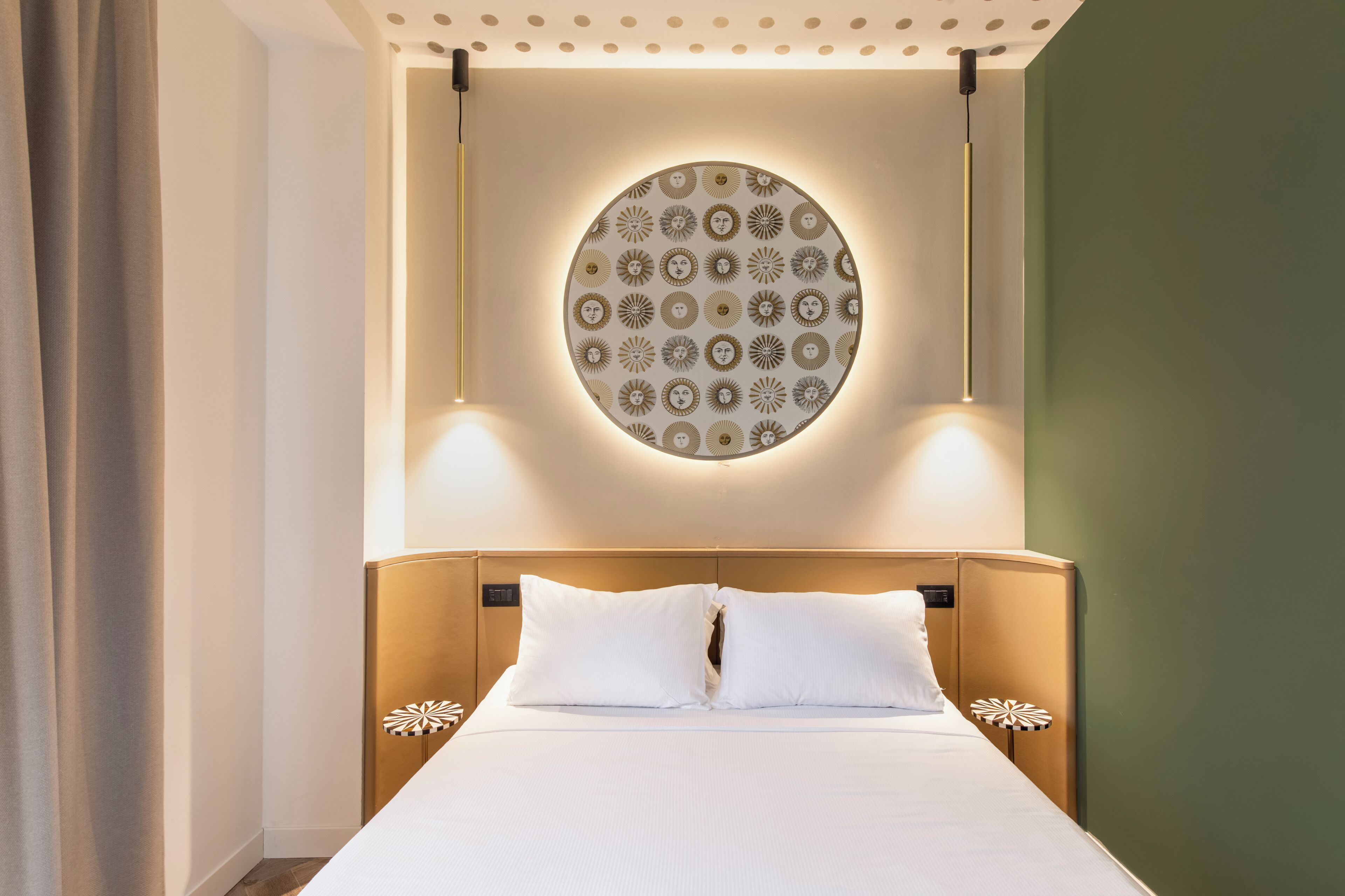 A hotel room with a bed, a circular wall decoration, and two wall-mounted lights.
