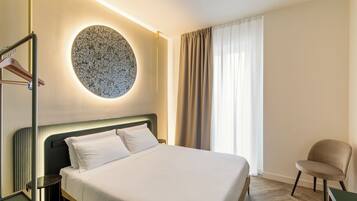 A hotel room with a bed, a round wall decoration, a chair, and a window with curtains.