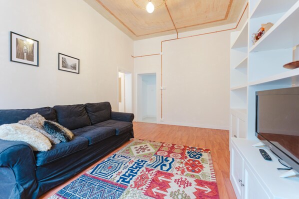 A living room with a dark sofa, a colorful rug, a television, and a white cabinet. - Elisa's Flat - 5 min from Train Station  (Mestre)