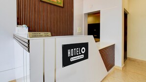 Ein Empfangsschalter mit Schild, das Ein- und Auscheckzeiten angibt, einem firmenzugehörigen Etikett und einem gerahmten Bild darüber.