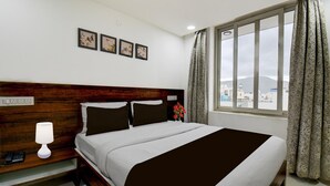 Ein Hotelzimmer mit einem großen Bett, einem Nachttisch mit Lampe, einem Beistelltisch und einem Fenster mit Vorhängen.