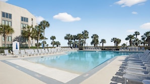 Una piscina con sillones de descanso, palmeras y un edificio al fondo.