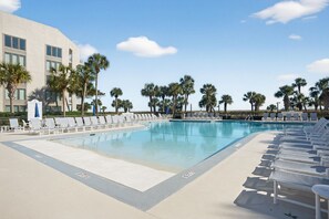 Ein Swimmingpool mit Liegestühlen, Palmen und einem Gebäude im Hintergrund.