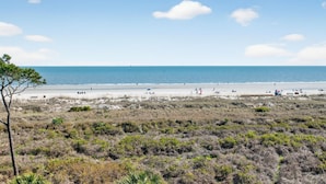 Una playa con gente, cielo despejado y vegetación escasa.