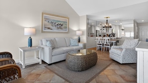 Una sala de estar moderna con un sofá, una mesa de centro y sillas, un comedor con una mesa y sillas, y una cocina al fondo.