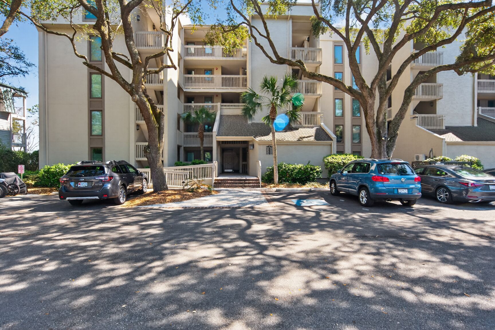 A multi-story residential building with a parking lot, trees, and parked cars.