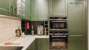 Una cocina con armarios verdes, un tostador, una cafetera y una cuchara de madera sobre la encimera.