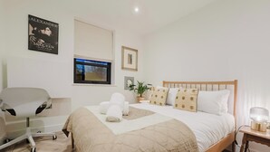 Un dormitorio ordenado con cama, una silla, un televisor y un cartel en la pared.