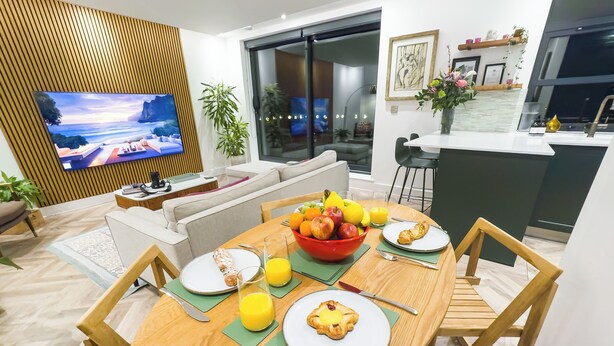 Una sala de estar moderna con televisor, sofá, mesa de comedor con desayuno y una zona de cocina.
