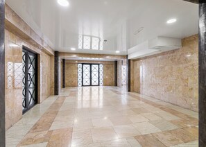Um hall amplo com piso de mármore, entrada por porta de vidro e teto com iluminação embutida.