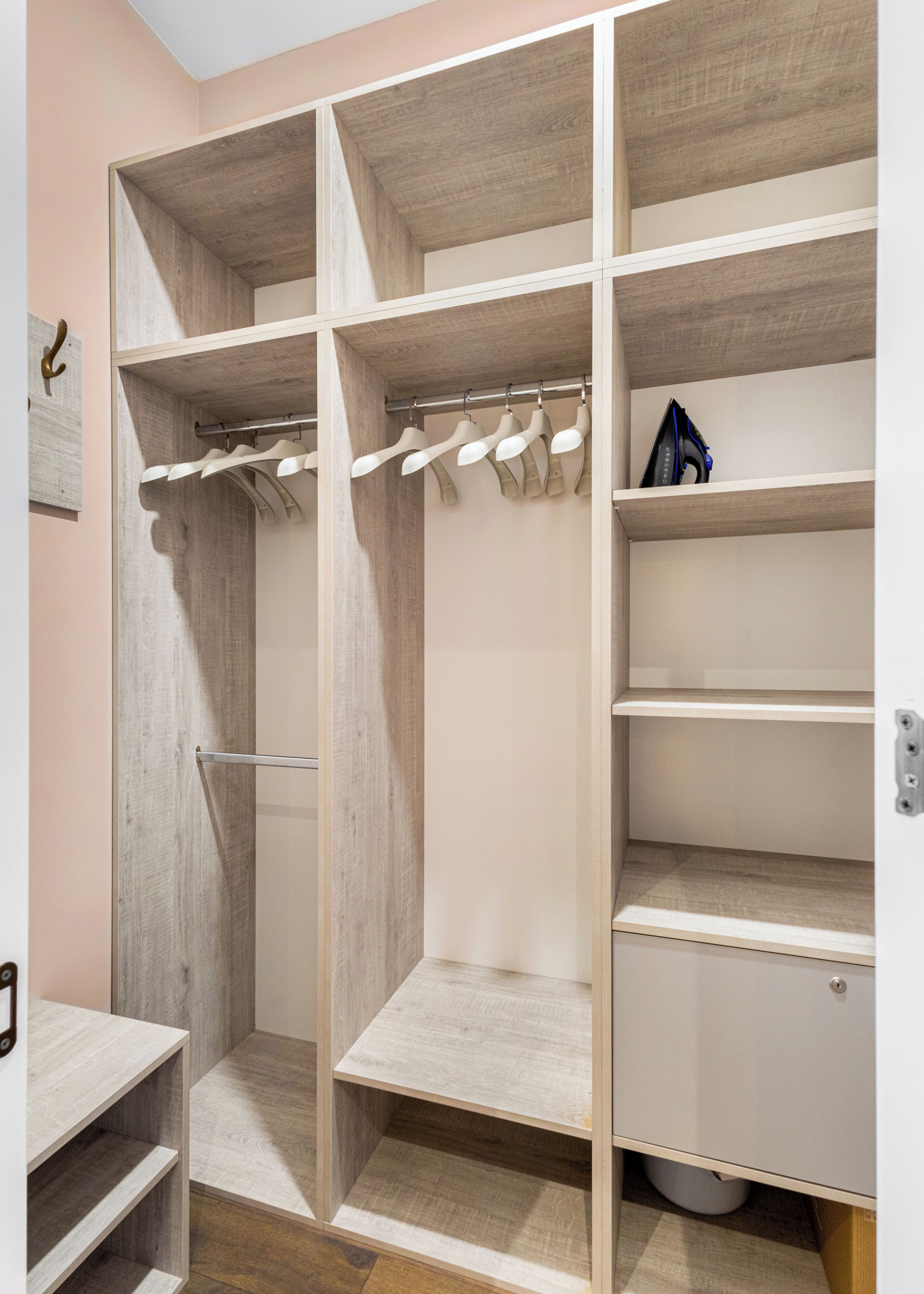 Ein begehbarer Kleiderschrank mit mehreren Regalen und Ablageflächen, einer Kleiderstange und einem kleinen Bügelbrett.