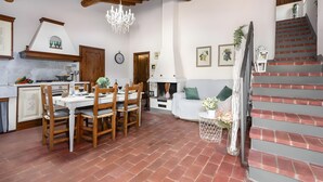 A spacious living area with a dining table, wooden chairs, a fireplace, and a staircase. - Apartment with Garden and Jacuzzi in Mugello (Barberino di Mugello)