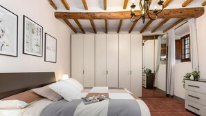 A bedroom with a bed, a dresser, a mirror, and a ceiling with exposed beams. - Apartment with Garden and Jacuzzi in Mugello (Barberino di Mugello)