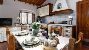 A dining area with a table set for four, a television, and a kitchen in the background. - Apartment with Garden and Jacuzzi in Mugello (Barberino di Mugello)