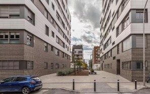 Eine moderne Stadtstraße mit mehrstöckigen Gebäuden, ein blaues Auto, das am Straßenrand geparkt ist, und einem klaren Himmel.