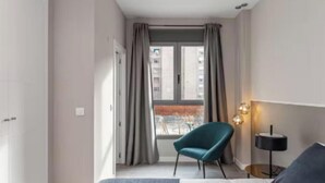 Een moderne hotelkamer met een groot raam, een blauwgroene fauteuil, een bedlamp en een bed.