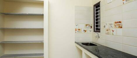 Una cocina con paredes de azulejos blancos, encimera negra y ventana con reja.
