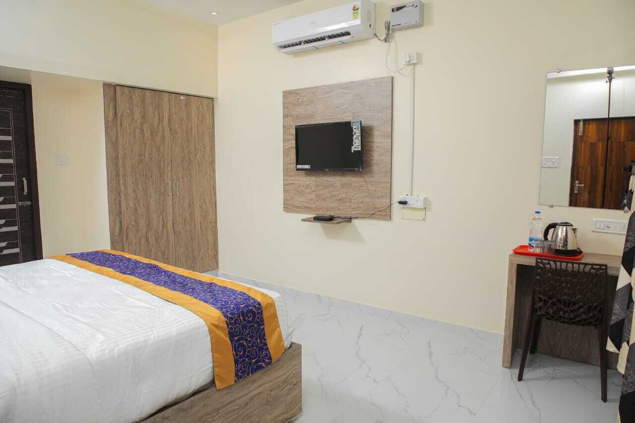 A hotel room with a bed, a desk with a chair, a TV mounted on the wall, and an air conditioning unit.