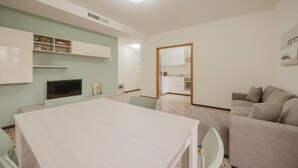 A modern kitchen with white cabinets, a dining table, and a grey sofa. - Vittoria's Flat - 15 min da Venezia (Mestre)