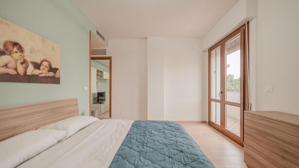 A bedroom with a bed, a blue blanket, a wooden headboard, a wooden wardrobe, a painting on the wall, and a sliding glass door leading to a balcony. - Vittoria's Flat - 15 min da Venezia (Mestre)