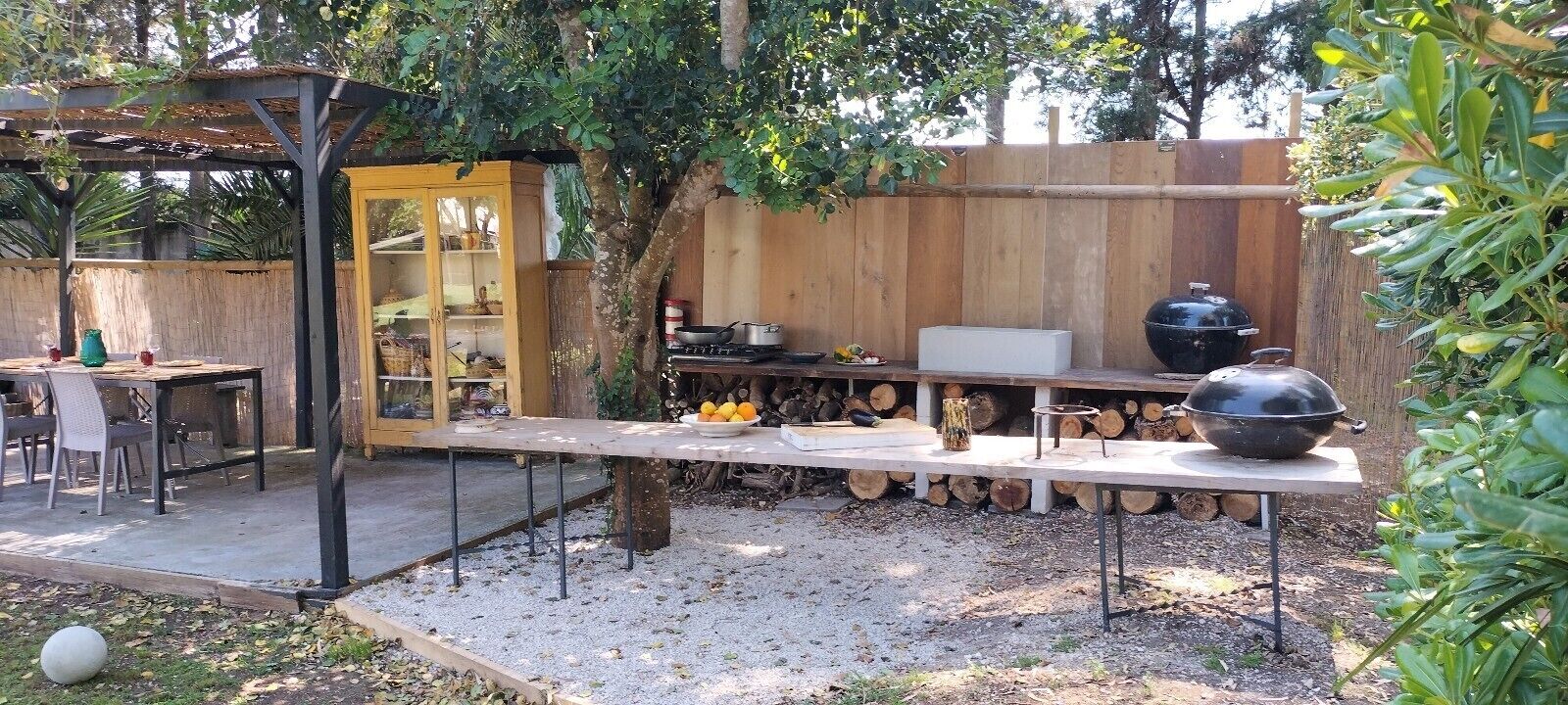 Um pátio externo com uma mesa de jantar, cadeiras, churrasqueira e cerca de madeira.