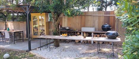Um pátio externo com uma mesa de jantar, cadeiras, churrasqueira e cerca de madeira.