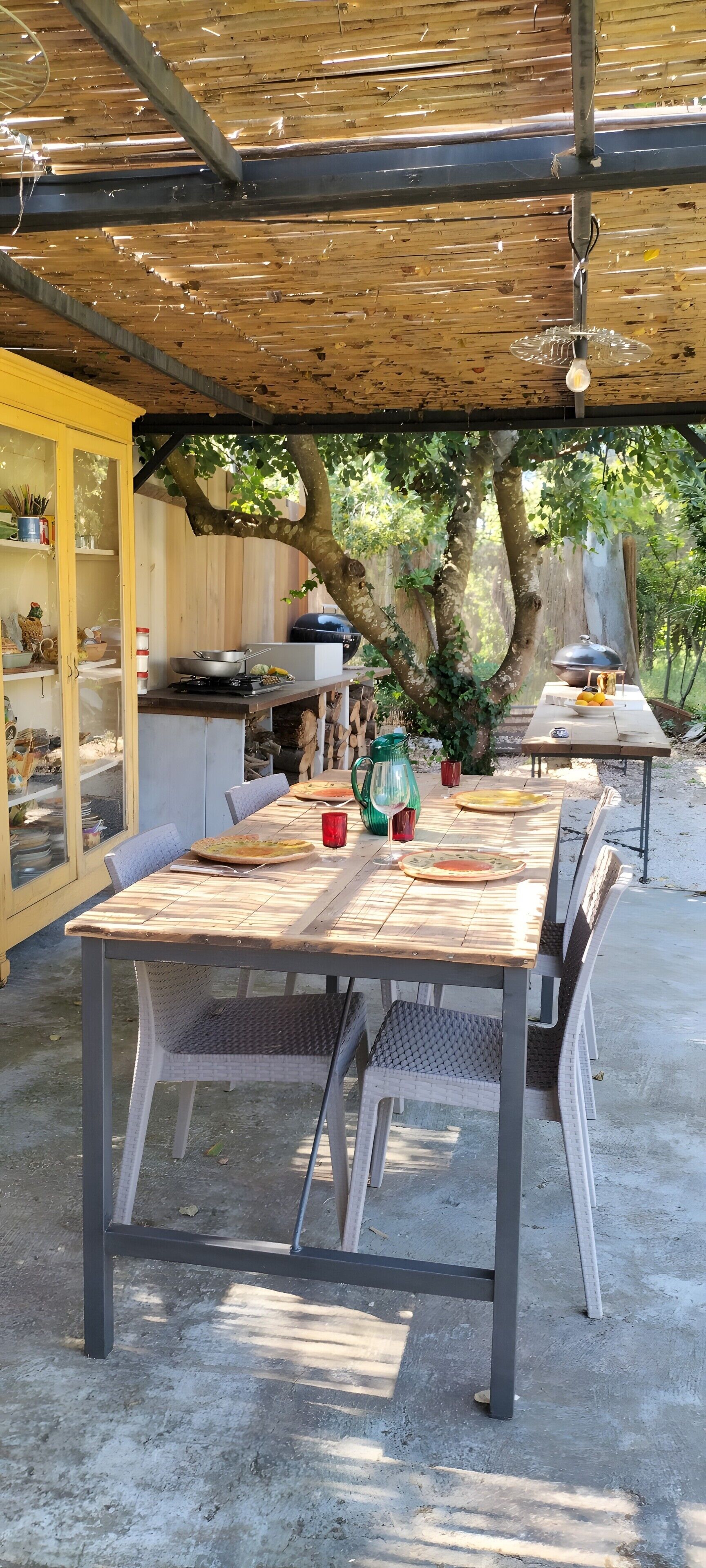 Un'area pranzo all'aperto con tavolo e sedie in legno, un barbecue e una zona salotto coperta.