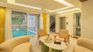 Una sala de estar moderna con vista a una piscina, dos sillones, una mesita de centro y un ventilador de techo.