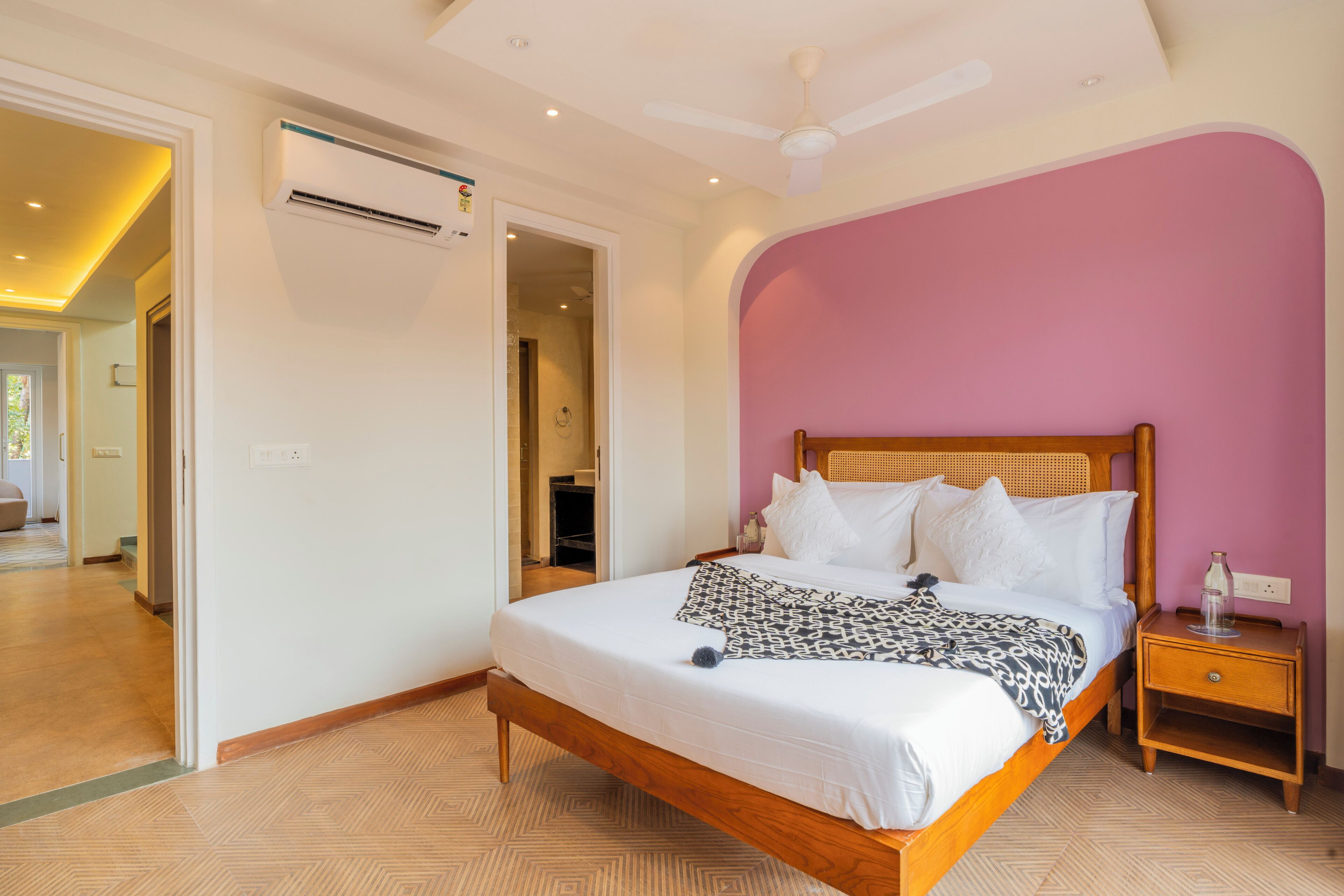 Een slaapkamer met een houten bed, wit beddengoed, een nachtkastje en een plafondventilator.