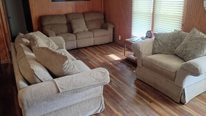 Una sala de estar con dos sofás beige, piso de madera, una mesita y una ventana con persianas.