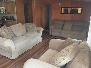 Ein Wohnzimmer mit zwei Sofas, Holzboden und einer Küchenzeile mit Schränken und Geräten.