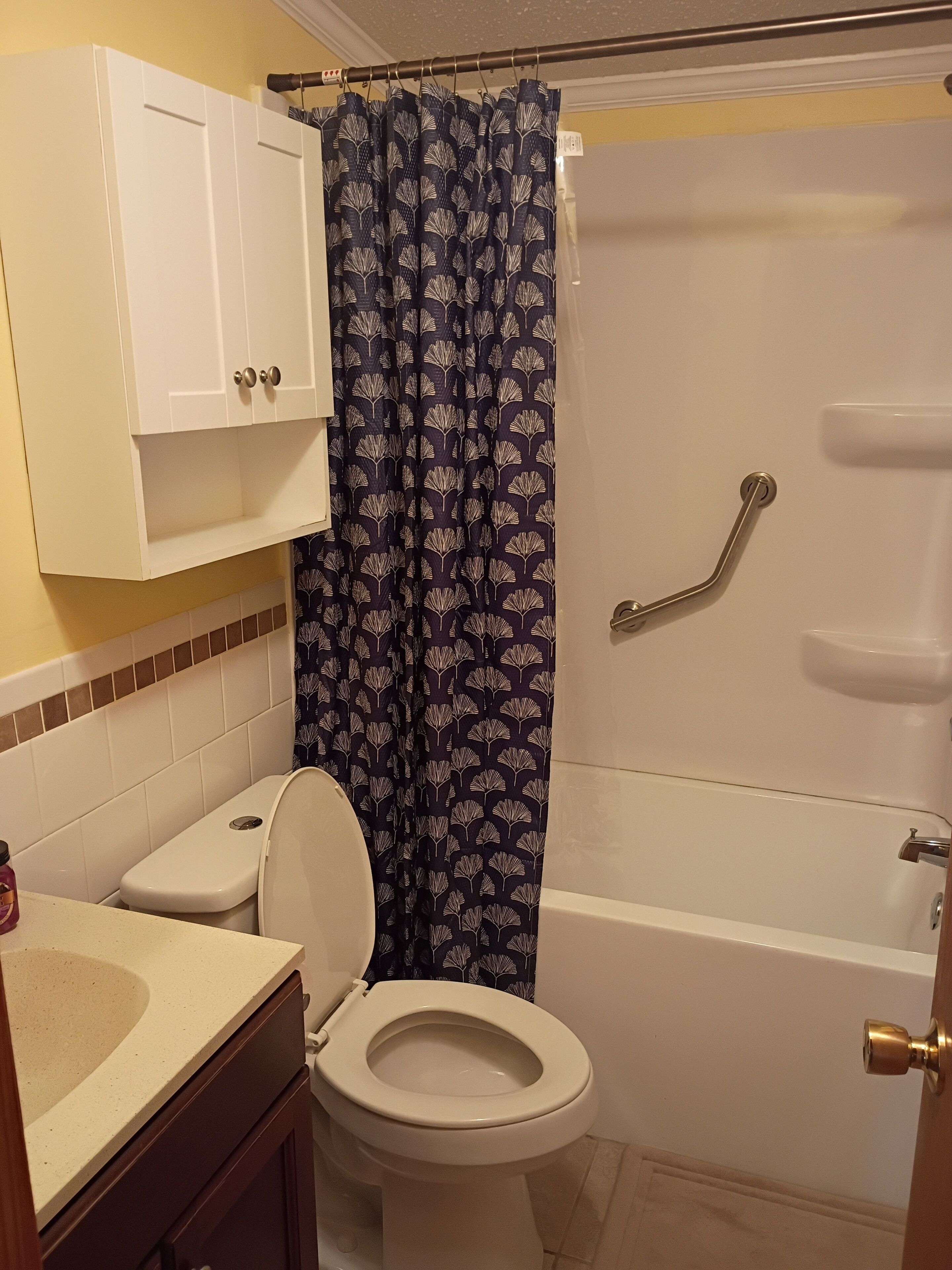 Un baño con inodoro, bañera, cortina de ducha, pasamanos y un armario.