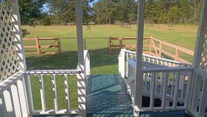 Una terraza de madera con barandillas blancas que da a un campo cubierto de césped.
