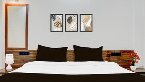 A hotel room with a wooden headboard, a large mirror, a bed with black and white bedding, and three framed wall art pieces.