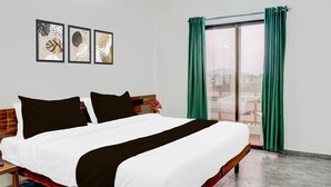 A hotel room with a bed, a wooden headboard, a large window with green curtains, and three framed wall art pieces.