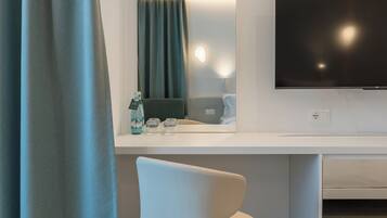 Ein modernes Hotelzimmer mit großem Flachbildfernseher, weißem Schreibtisch, Stuhl, Spiegel und Vorhang.