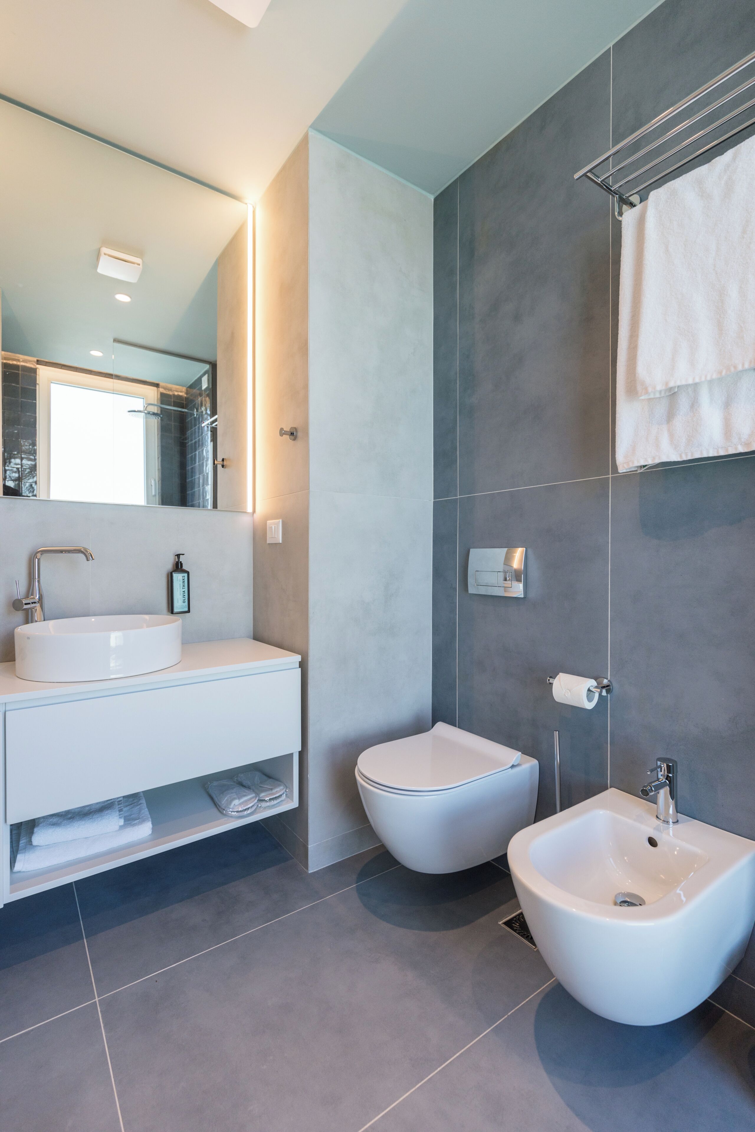 A modern bathroom with a white sink, bidet, and towel rack.