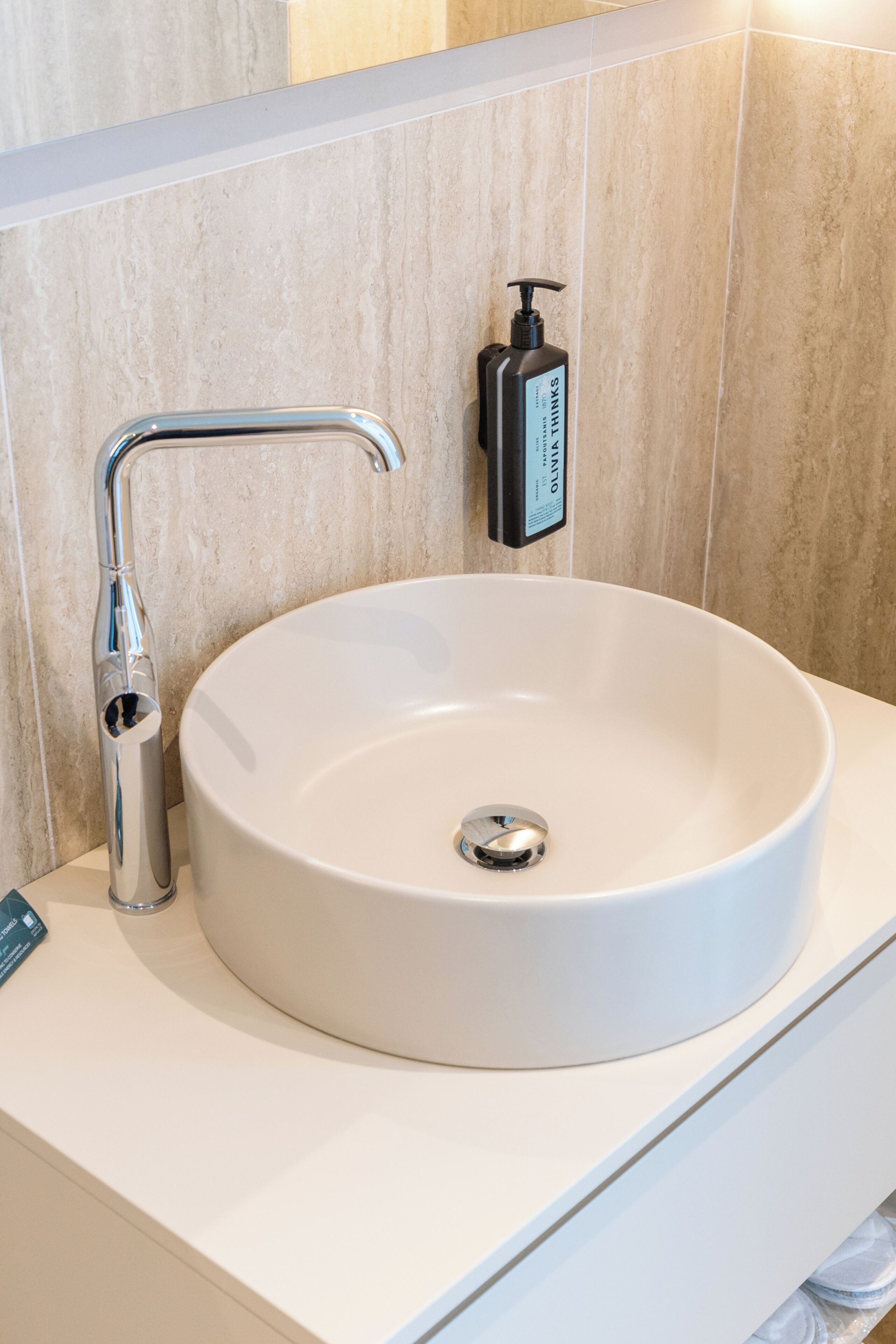 A bathroom with a white sink, chrome faucet, and a soap dispenser on the wall.