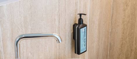 A bathroom with a white sink, chrome faucet, and a soap dispenser on the wall.