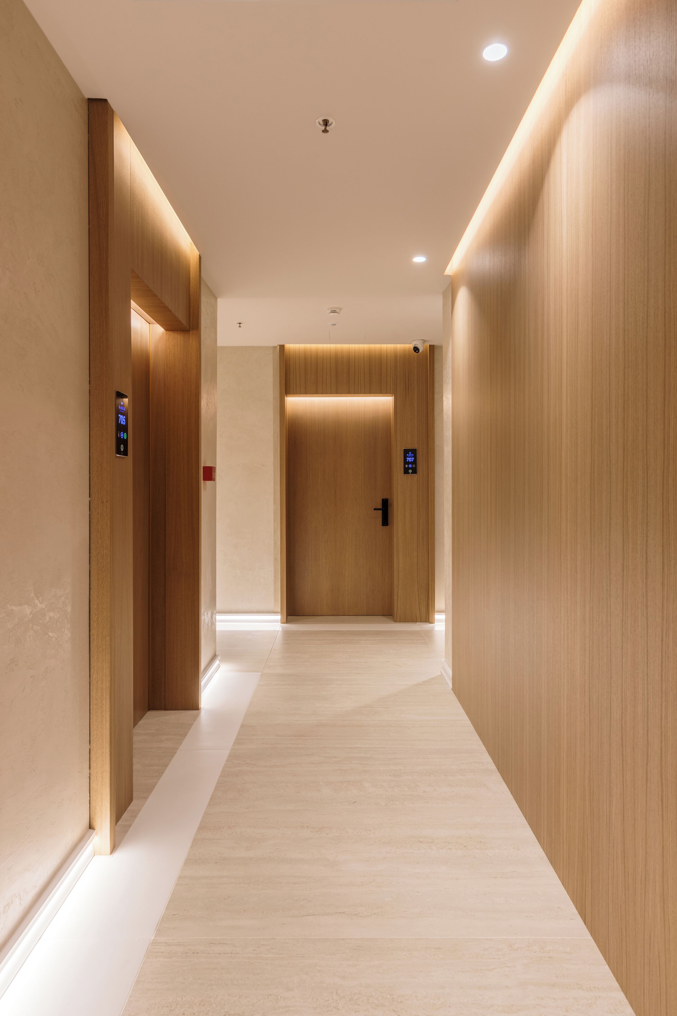 A modern hallway with wooden walls and a light-colored floor, leading to an elevator.