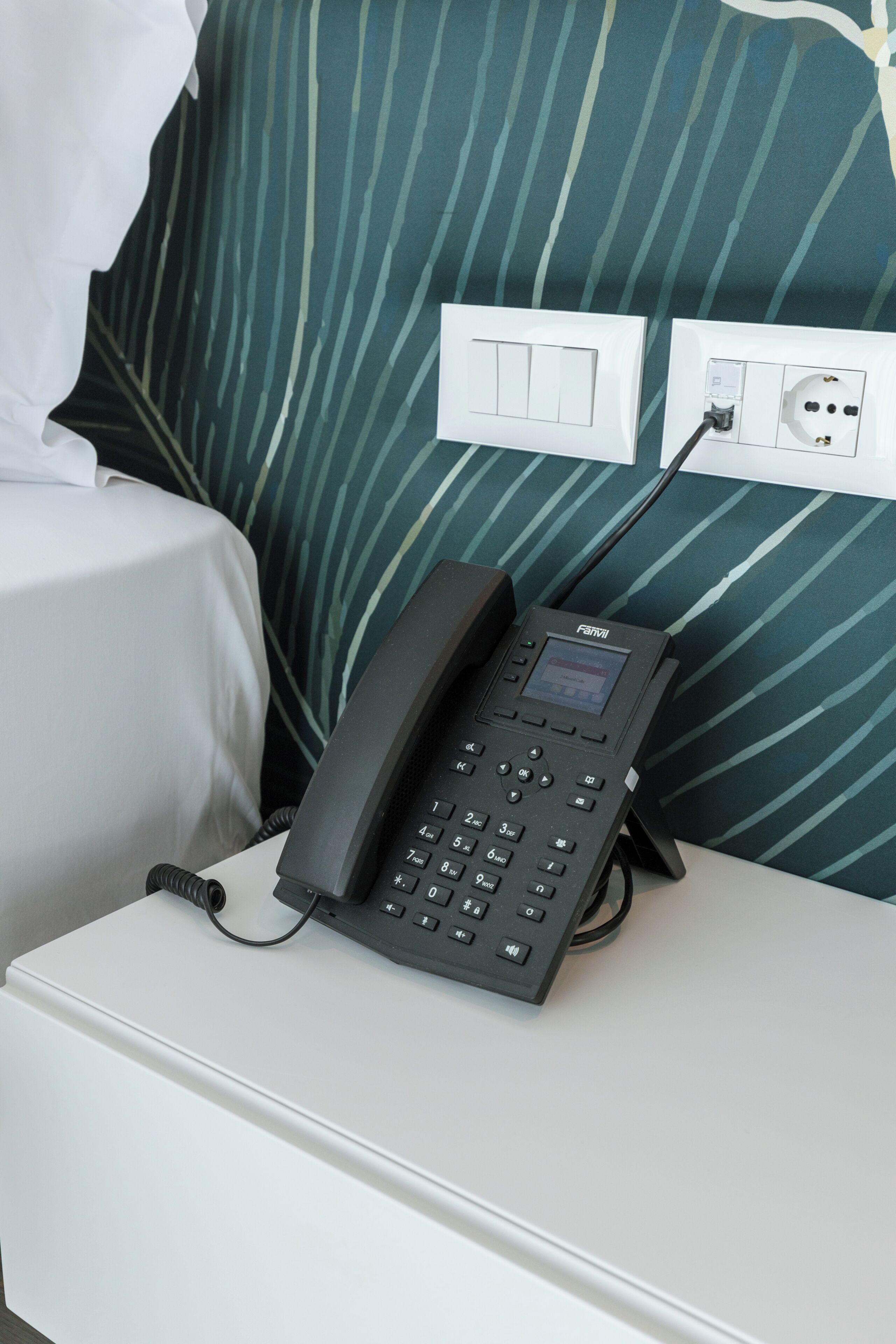 A hotel room with a bedside phone, a power outlet, and a bed with a striped pillow.