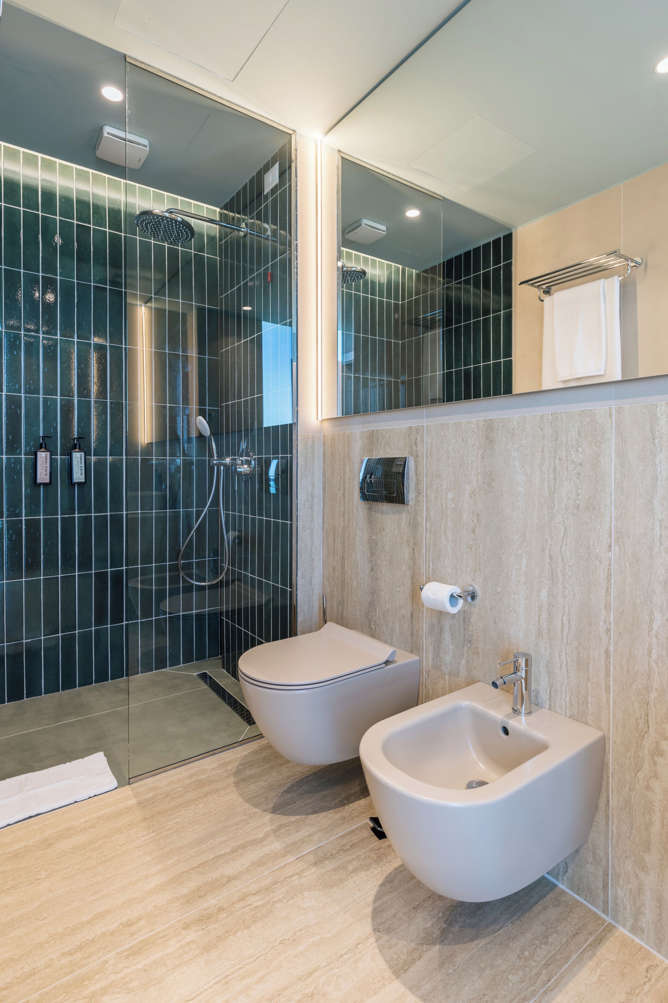 A modern bathroom with a glass-enclosed shower, a bidet, and a toilet.