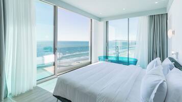 A modern hotel room with a large bed, a glass table, and a view of the ocean.